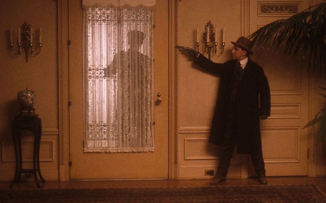 Film still from THE GODFATHER PART II: A man waits in a house behind the door with his gun drawn.