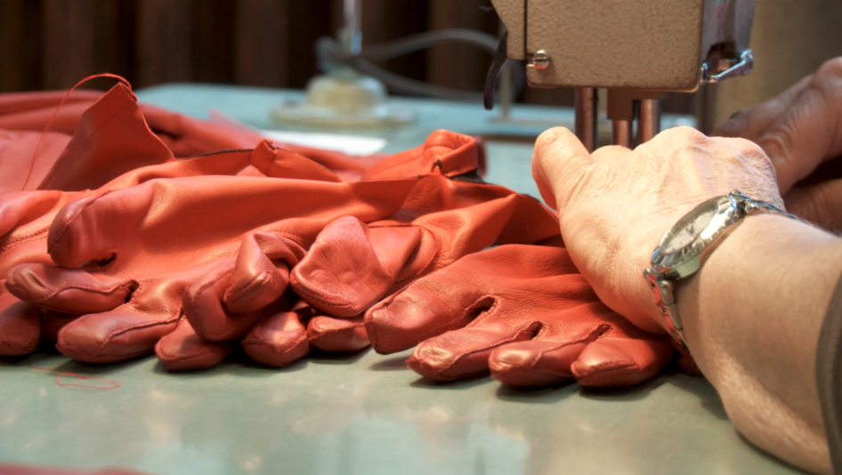 Film still from THE UNSTABLE OBJECT: Red leather gloves are sewn on a sewing machine.