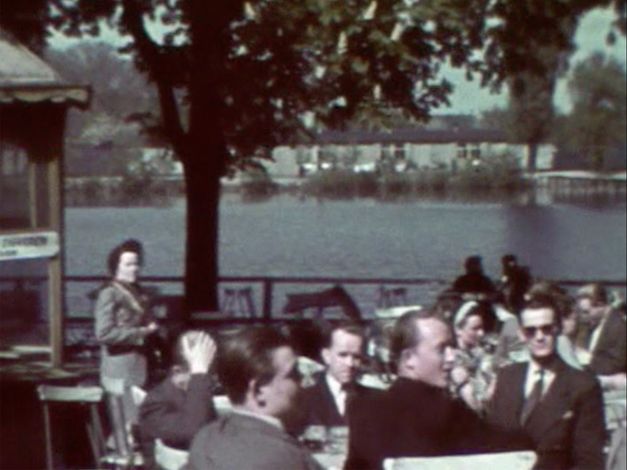 People sitting in a beer garden. Water in the background, the sun is shining.