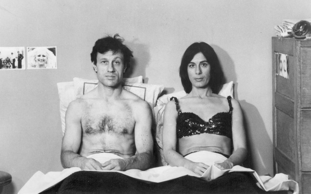 Film still from KRISTINA TALKING PICTURES: A man and a woman sit next to each other in bed and look head-on into the camera.