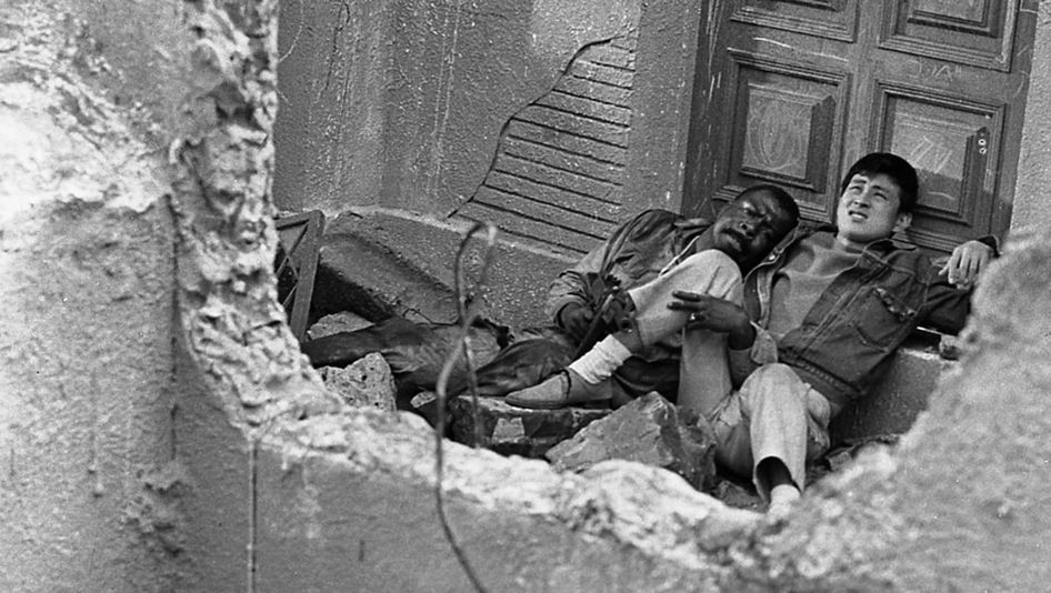 Film still from BLACK SUN: Two men, one of them Japanese, the other an African-American soldier, are sitting in a bombed-out house.