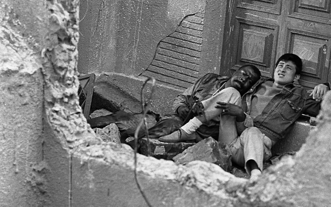 Film still from BLACK SUN: Two men, one of them Japanese, the other an African-American soldier, are sitting in a bombed-out house.