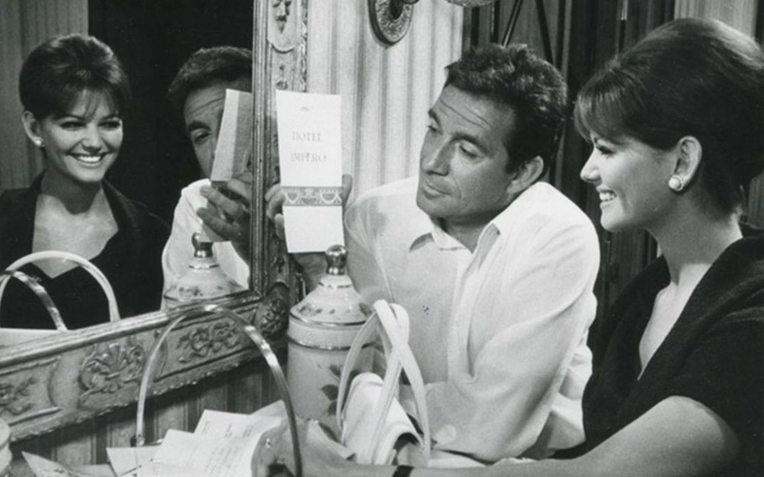 Film still from IL MAGNIFICO CORNUTO: A woman and a man sit laughing in front of a mirror.