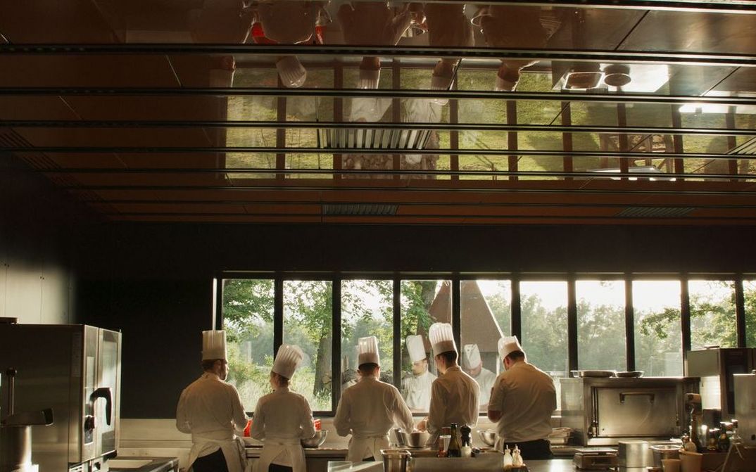 Film still from MENUS PLAISIRS: Five chefs stand next to each other in the kitchen. They can be seen twice through a reflection.