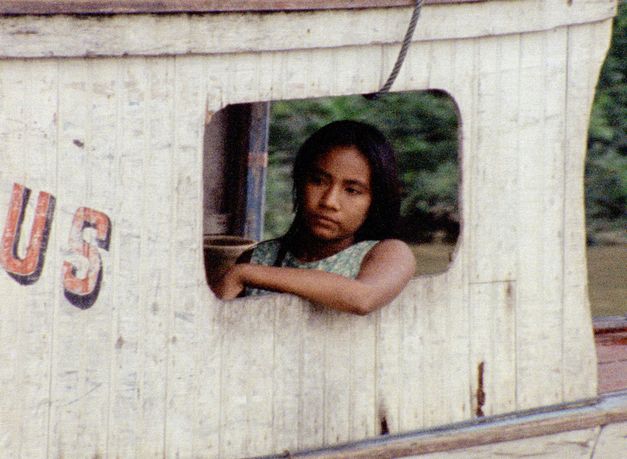 Film still from IRACEMA, UMA TRANSA AMAZÔNICA by Jorge Bodanzky and Orlando Senna. A young woman sits on the deck of a boat. Parts of an inscription, the letters US, can be seen on the outer paneling.