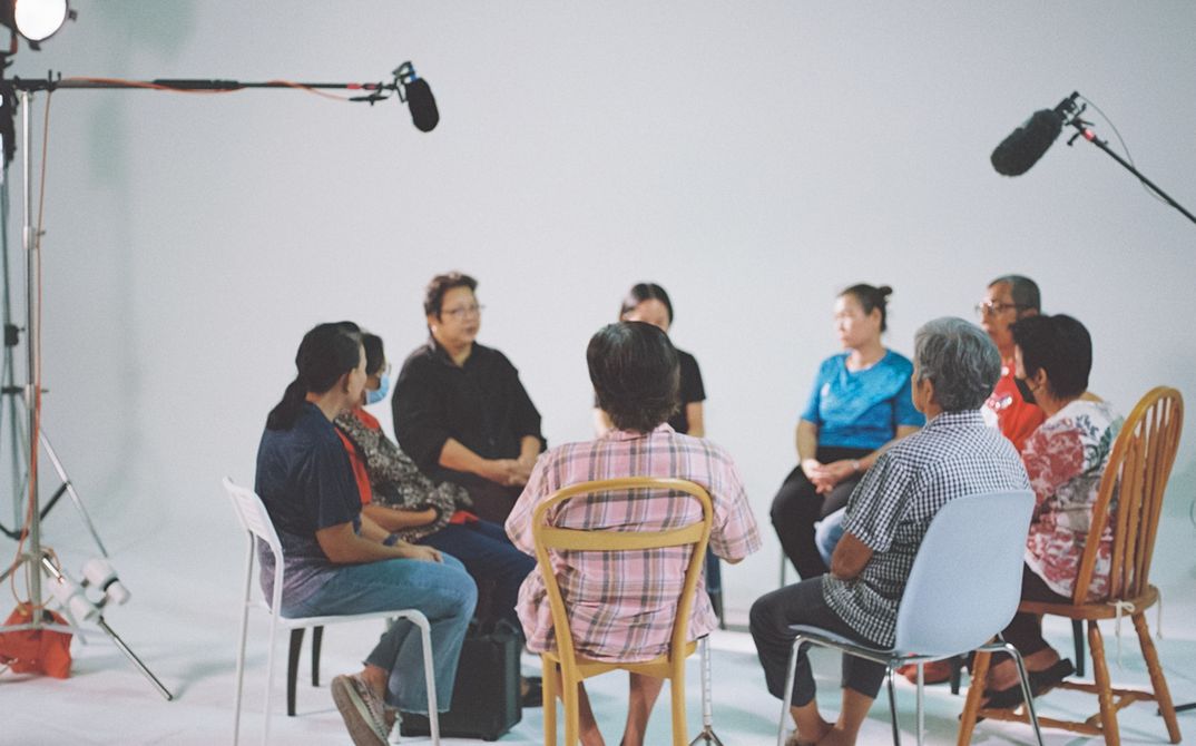 People sit in a film studio in a circle on different chairs.