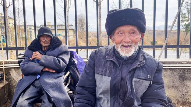 Film still from GUOCHANG by Nana Xu. The picture shows two elderly men in front of a fence.