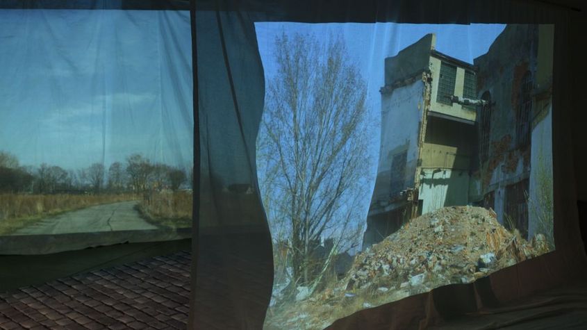 Still from the film "The Song of the Shirt" by Kerstin Schroedinger. Transparent fabric gives a glimpse of a crumbling house.