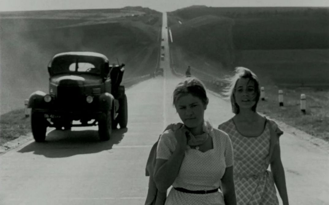 Film still from BRIEF ENCOUNTERS: Two young women dressed in summer clothes are walking down a street. A lorry can be seen behind them.