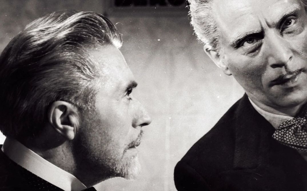 Film still from LA FIN DU JOUR: You can see the heads of two men, one is looking at the other.