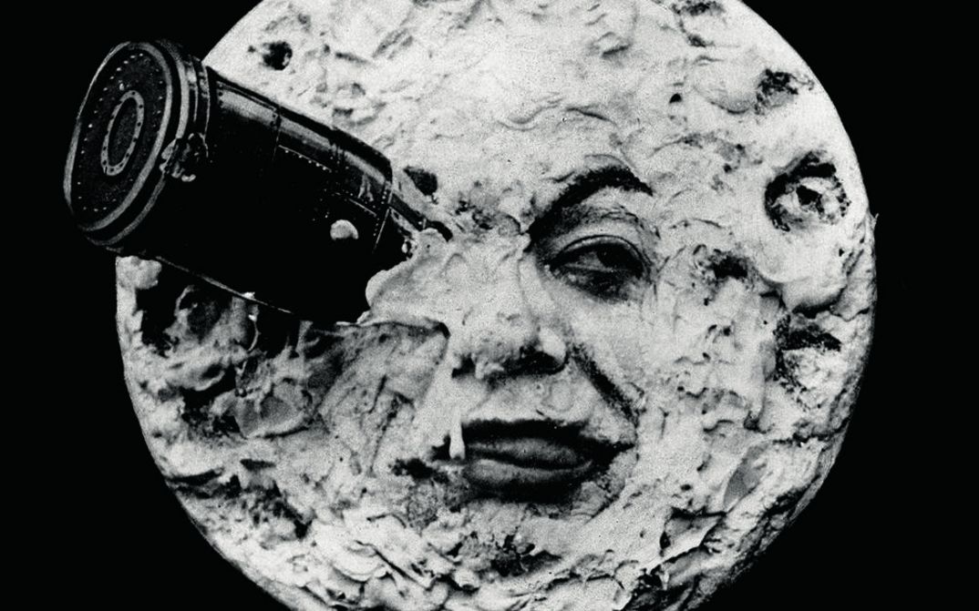 Film still from LE VOYAGE DANS LA LUNE: The moon as a human face with binoculars stuck in one eye.