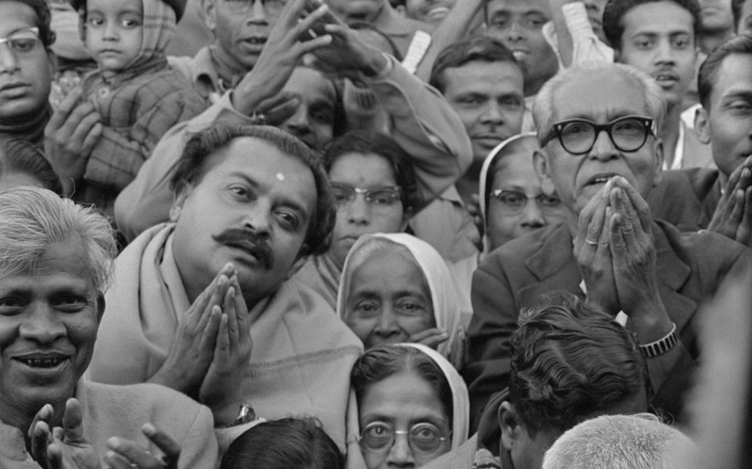 Filmstill from MAHAPURUSH: People are standing close together, looking upwards and holding hands, sometimes together.