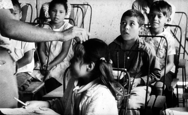 Filmstill aus POR PRIMERA VEZ: Eine Gruppe von Kindern hört jemandem zu.
