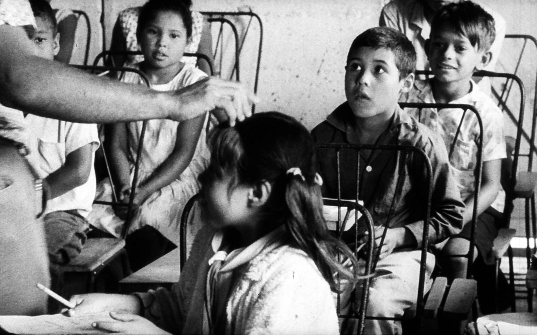 Film still from POR PRIMERA VEZ: A group of children are listening to someone.