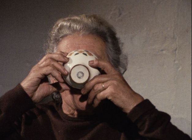 Film still from O MOVIMENTO DAS COISAS: A woman drinks from a cup that covers part of her face.