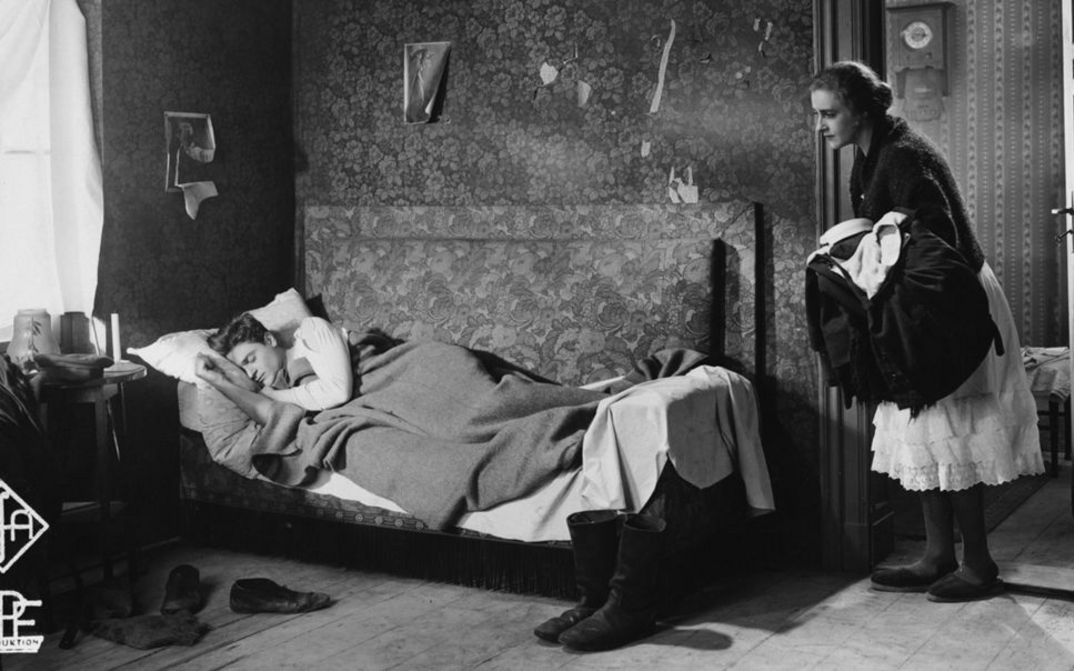 Film still from ZUFLUCHT. A woman looks into a room where a man is sleeping in bed.