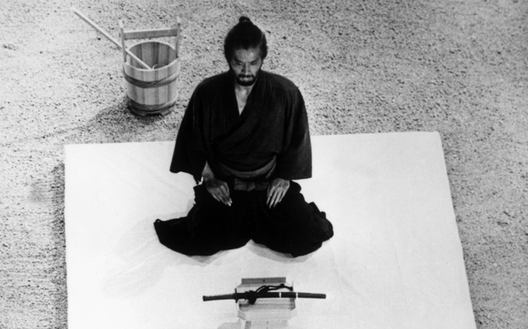 Film still from HARAKIRI: A man in a black kimono kneels in front of a sword.