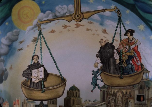 Film still from COPYRIGHT BY LUTHER: A drawing in colour. You can see a weighing pan in which church representatives and a royal person are sitting. A blue animal hangs from a bowl.