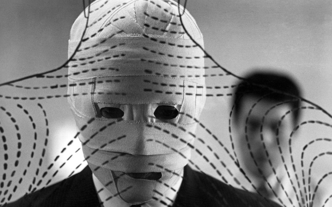 Film still from THE FACE OF ANOTHER: A man with a bandaged face stands in front of a transparent wall on which lines and strokes have been drawn.