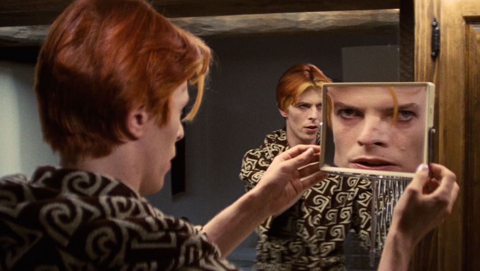 Filmstill aus THE MAN WHO FELL TO EARTH: David Bowie betrachtet sich gleichzeitig in einem großen und einem kleinen Spiegel, so dass er dreimal zu sehen ist.