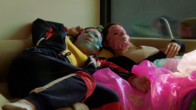 Two girls with face masks are lying on a bed in a teenager