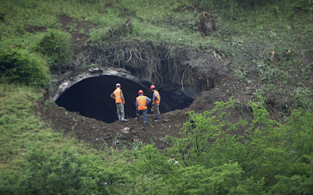 Filmstill aus A TUNNEL. Drei Männer in Arbeitskleidung schauen in eine Tunnelöffnung inmitten einer grünen Landschaft.