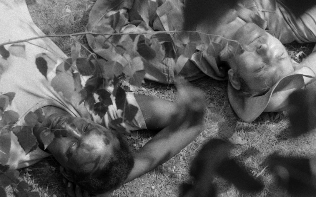 Film still from JAGDPARTIE: A black man and a white man are lying next to each other in the grass.