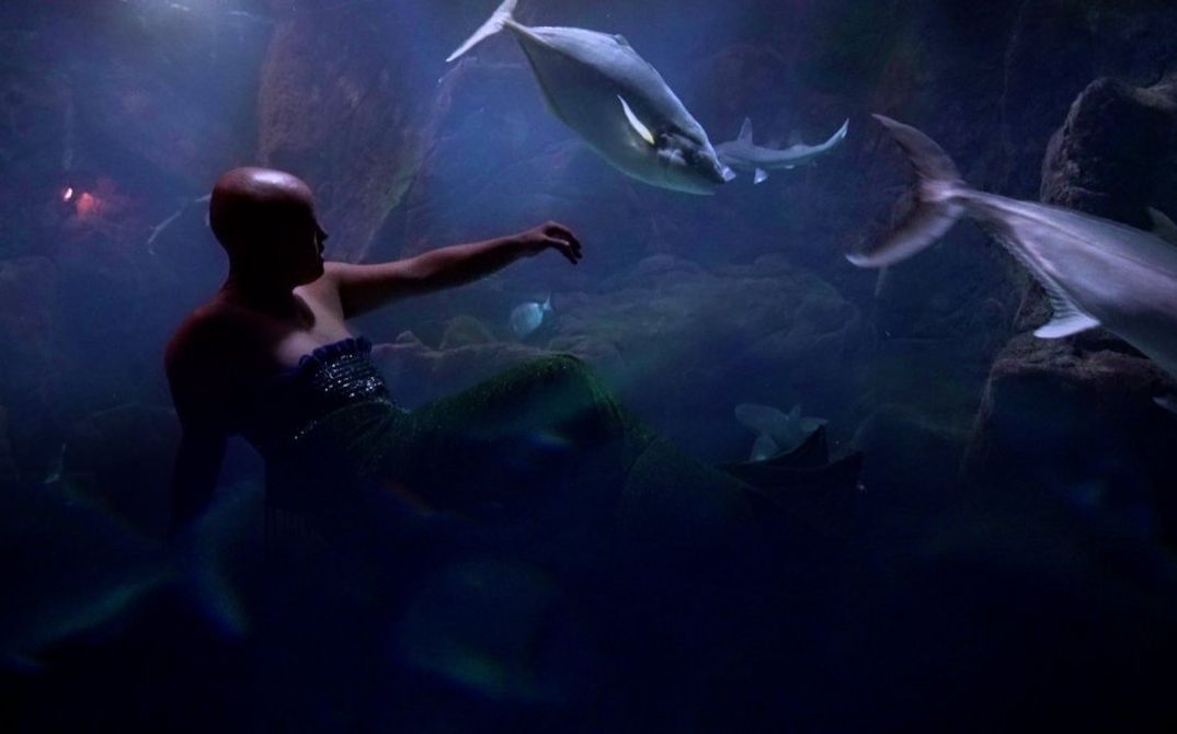 Still from "Super Natural": A hairless mermaid on the bottom of the sea, surrounded by fish