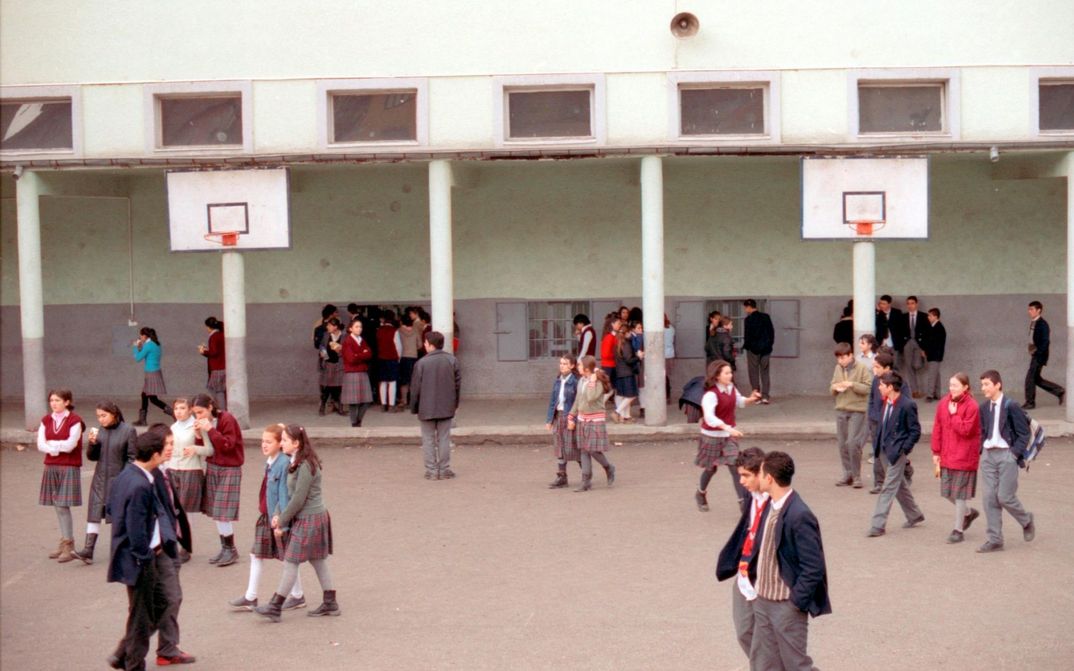 Filmstill from AUS DER FERNE: A school playground with lots of pupils in school uniform. There are also two basketball hoops.
