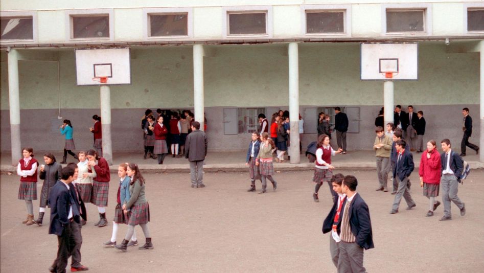 Filmstill from AUS DER FERNE: A school playground with lots of pupils in school uniform. There are also two basketball hoops.