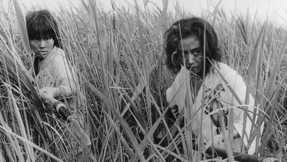 Film still from ONIBABA: Two women, armed with spears, stand in an attack position in a field full of reeds.