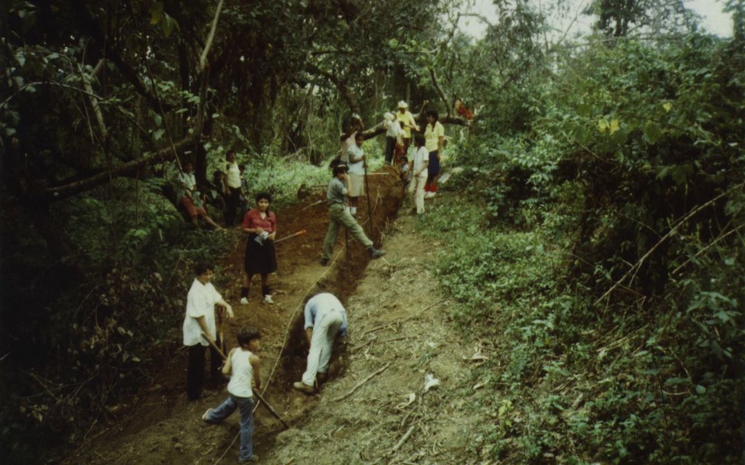 Filmstill from BRIEFE AUS WIWILLI: People dig a furrow in a slope. Around them is forest.