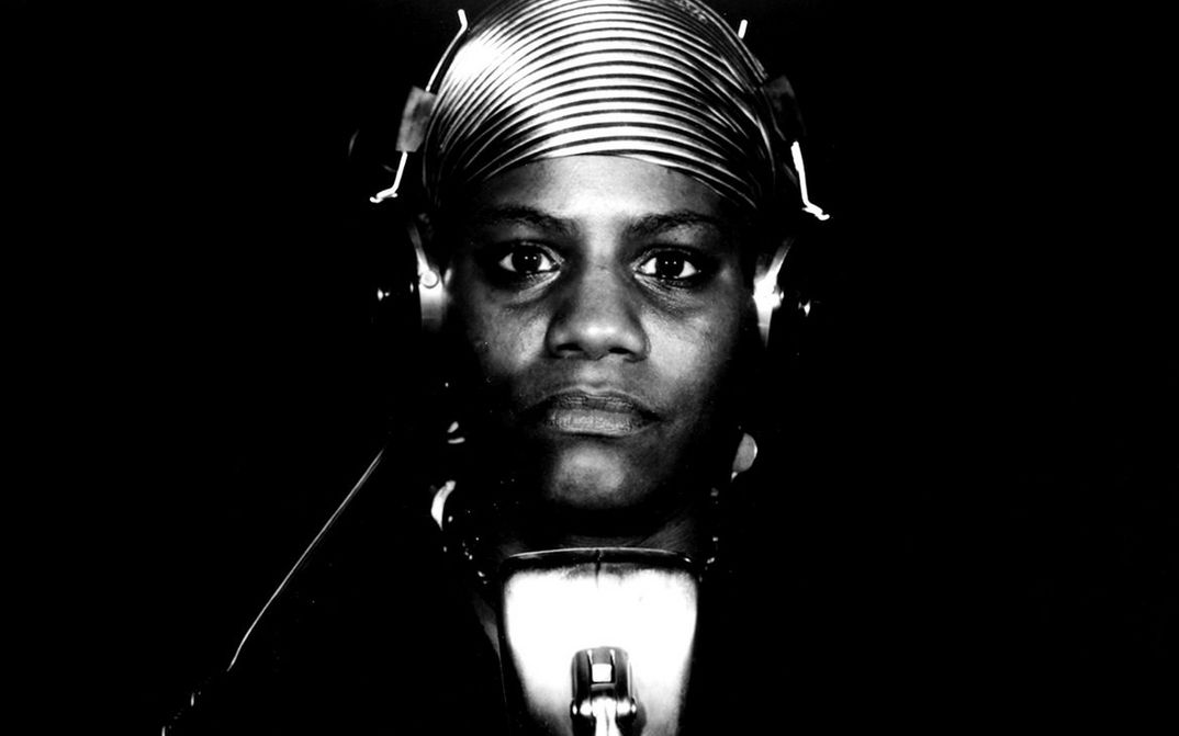 Filmstill aus BORN IN FLAMES: Eine Frau sitzt mit Kopfhörern im Radiostudio vor einem Mikrofon.vor eine