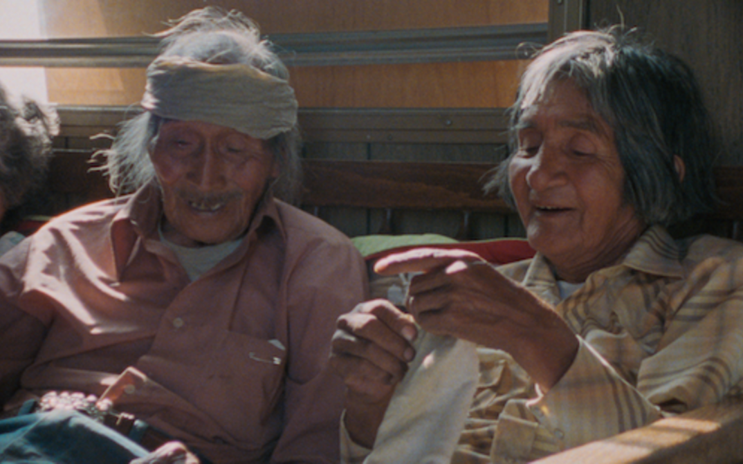 Film still from Techqua Ikachi – Land, mein Leben: It shows an old man and an old woman sitting next to each other.