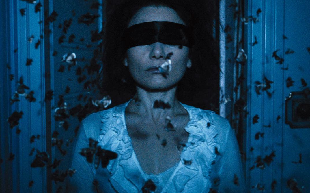 Film still from THE DUKE OF BURGUNDY: A blindfolded woman surrounded by butterflies.