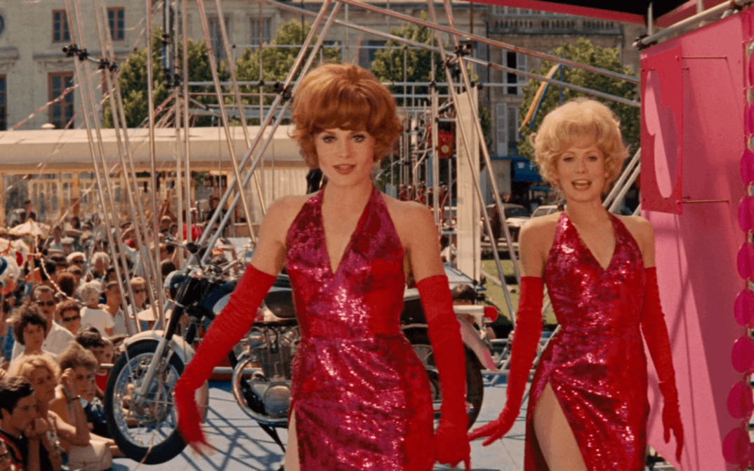 Filmstill aus LES DEMOISELLES DE ROCHEFORT: Zwei junge Frauen in roten Paillettenkleidern tanzen auf einem Volksfest.