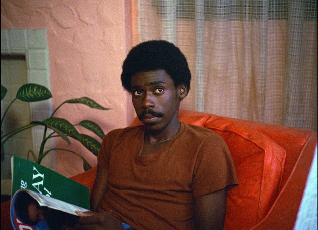 Mann sitzt auf einem Sessel und hält ein offenes Buch in den Händen.