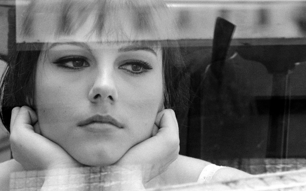 Film still from IO LA CONOSCEVO BENE: A young woman gazes thoughtfully out of the window, resting her face in her hands.