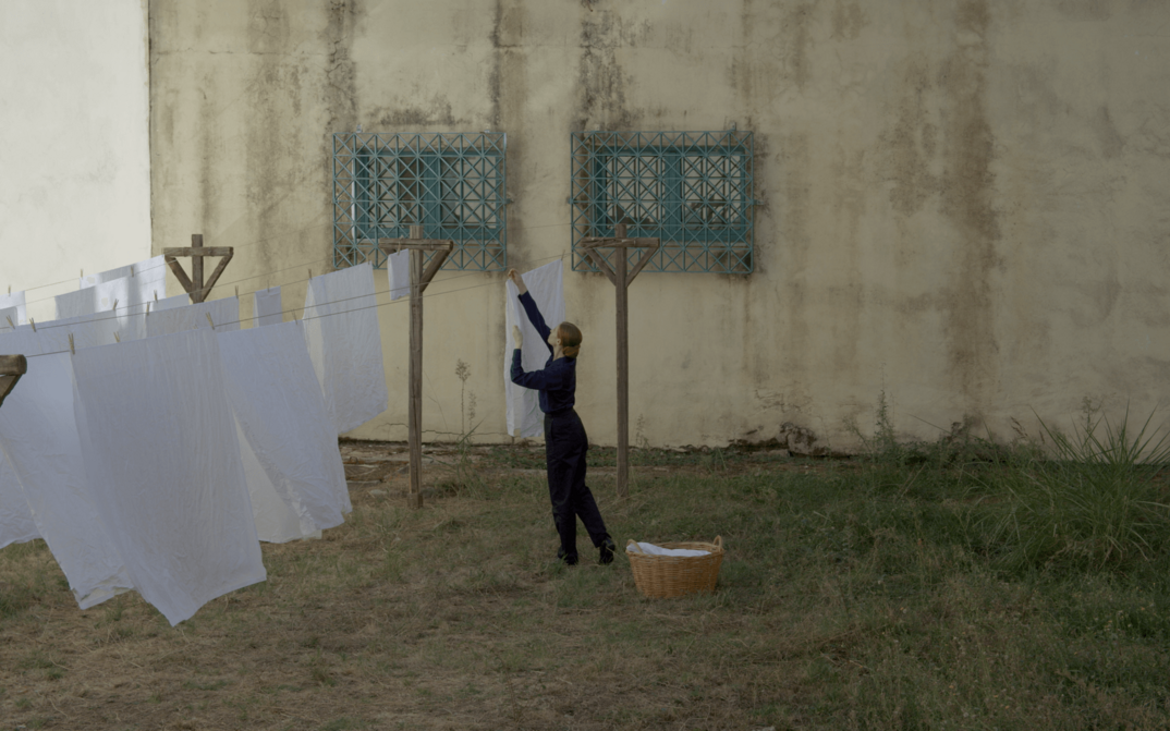 Film still from MUSIC: A woman hangs laundry outdoors.