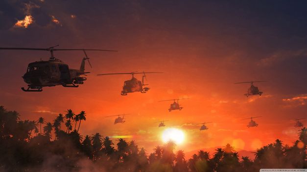 Film still from APOCALYPSE NOW: Several helicopters fly over palm trees in an orange sky.