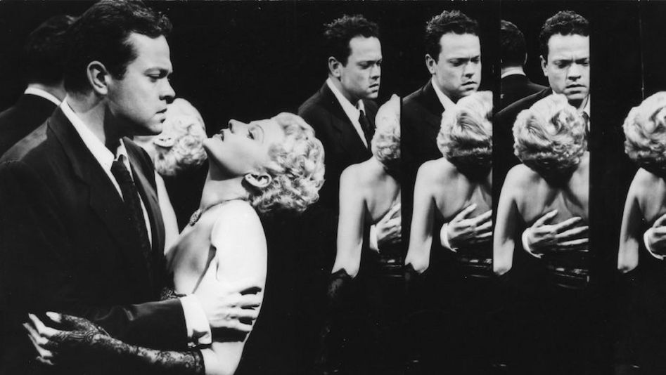 Film still from THE LADY FROM SHANGHAI: A man holds a woman in his arms, she tilts her head back. They are in a hall of mirrors and mirrored several times.