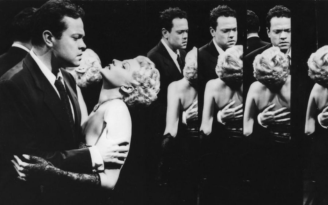 Film still from THE LADY FROM SHANGHAI: A man holds a woman in his arms, she tilts her head back. They are in a hall of mirrors and mirrored several times.