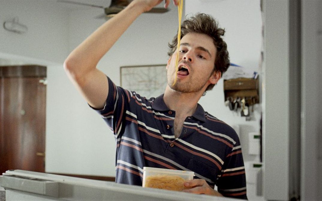 Filmstill from the movie "Arturo a los 30" by Martín Shanly. A young man is eating noodles from a tupperware with his hands.