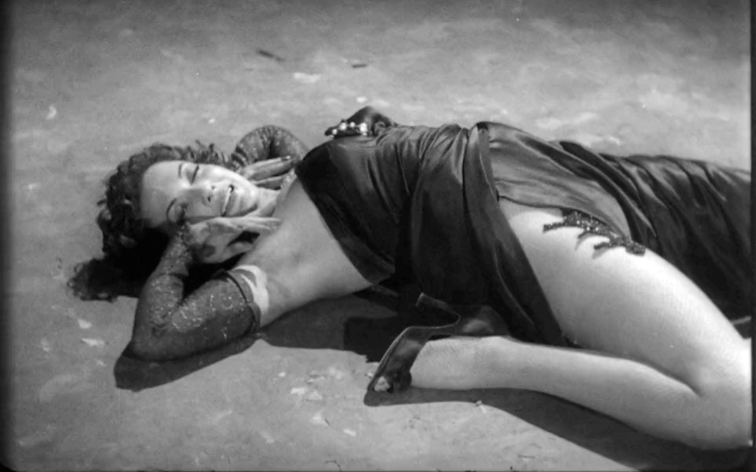 Film still from MÁS FUERTE QUE EL AMOR: A woman in an evening dress lies strangely contorted on the floor.