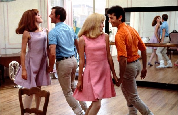 Filmstill from LES DEMOISELLES DE ROCHEFORT: Two couples in brightly coloured dresses dance lively together in a dance studio.