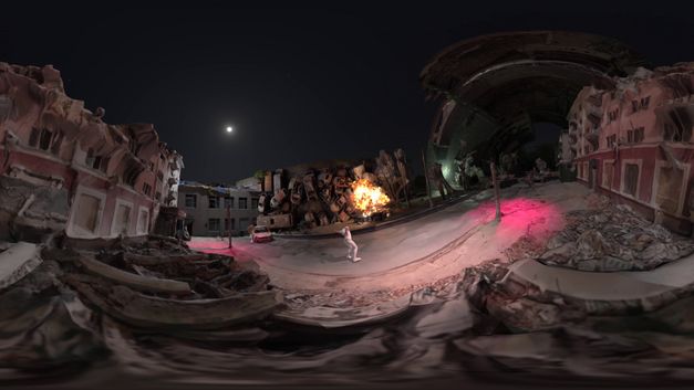 Filmstill aus dem Film „RAPTURE“ von Alisa Berger. Diese 360-Grad-Panoramaszene ist eine virtuelle Nachbildung einer nächtlichen, apokalyptischen Umgebung. Die 3D-Modellierung zeigt teilweise eingestürzte Gebäude. Im Zentrum der virtuellen Umgebung ist eine Explosion oder ein Feuer zu sehen. Rosa/rote Lichteffekte werden auf den Boden projiziert. Ein in Weiß gekleideter Avatar steht in der Straße.