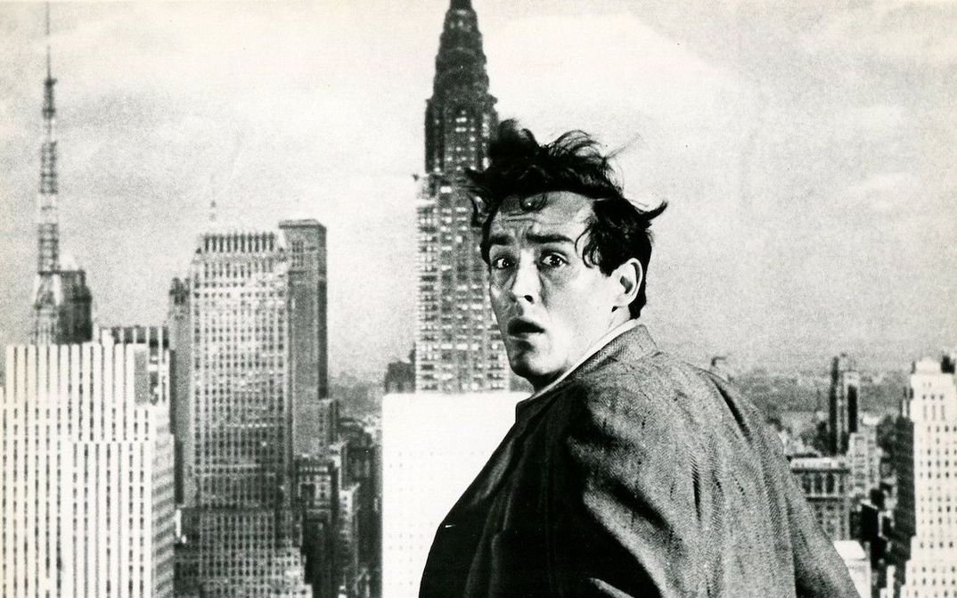 Film still from THE GLASS WALL: A man turns to the camera with a frightened expression on his face. The skyscrapers of New York can be seen behind him.