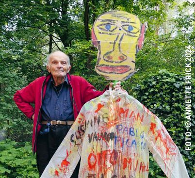 Film still from DAS GROSSE UND DAS KLEINE TOHUWABOHU: The filmmaker Wilhelm Hein stands next to a man-sized figure with a cardboard head and a colorfully smeared shirt.