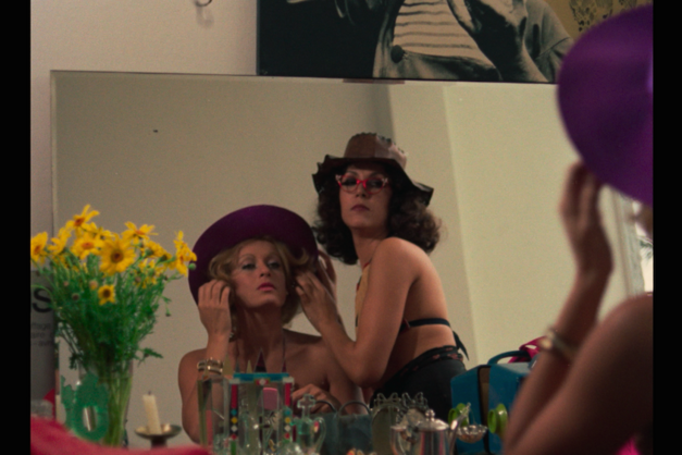 Film still from THE MAN I LOVED: Two women in beachwear and hats look at themselves in a mirror.