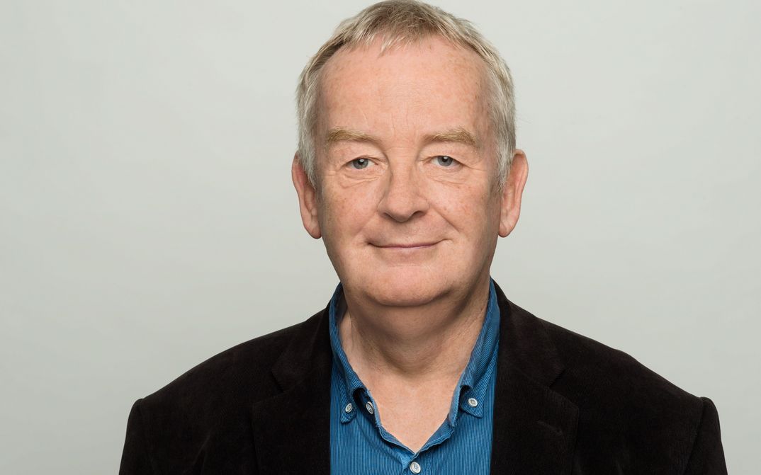 Portrait picture of Ralf Schenk. He wears a jacket and blue shirt and smiles at the camera.